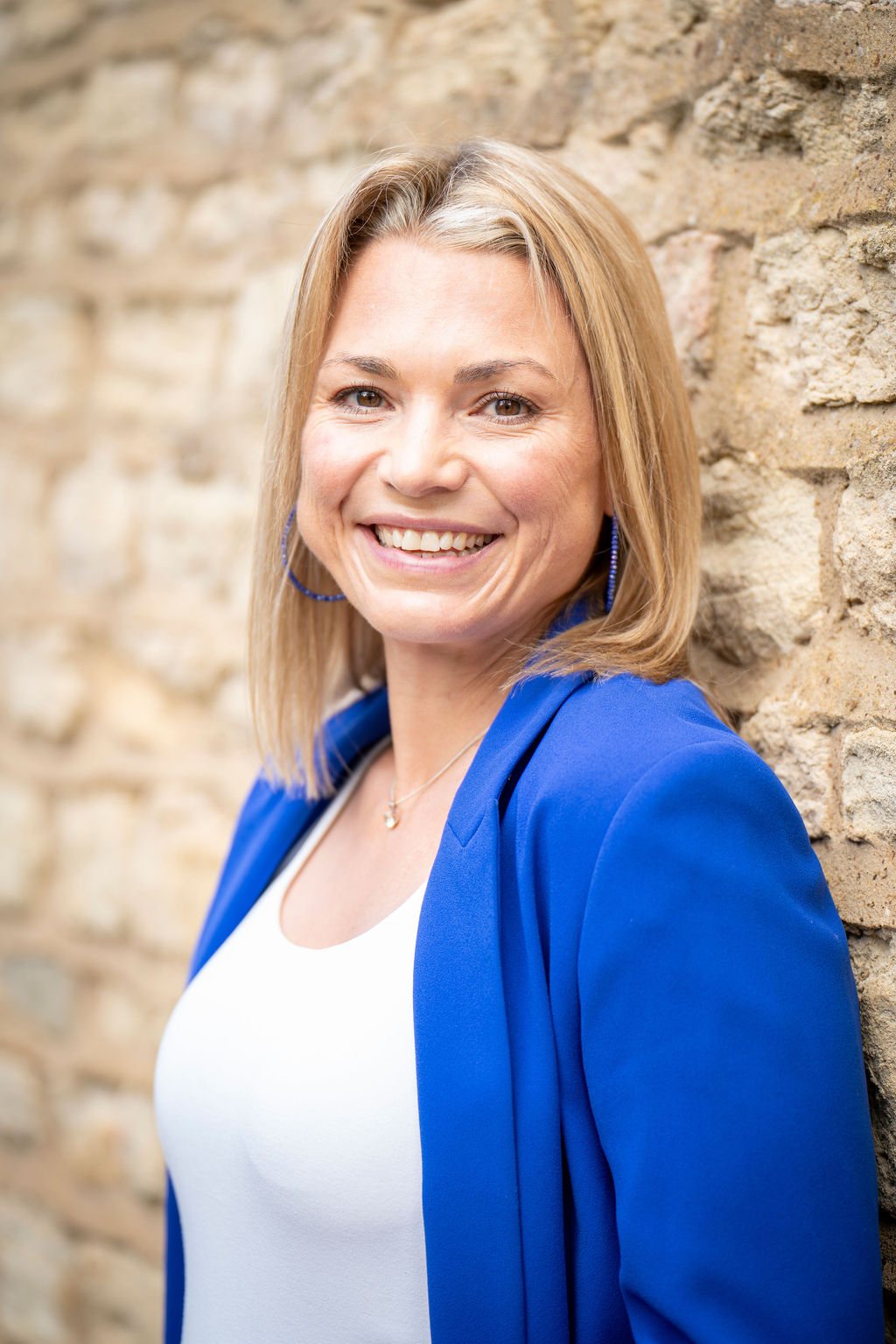 Charley Southon standing against a stone wall in a blue jacket